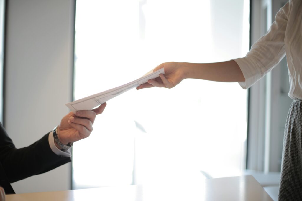 Image of a person handing another person a small stack of papers.